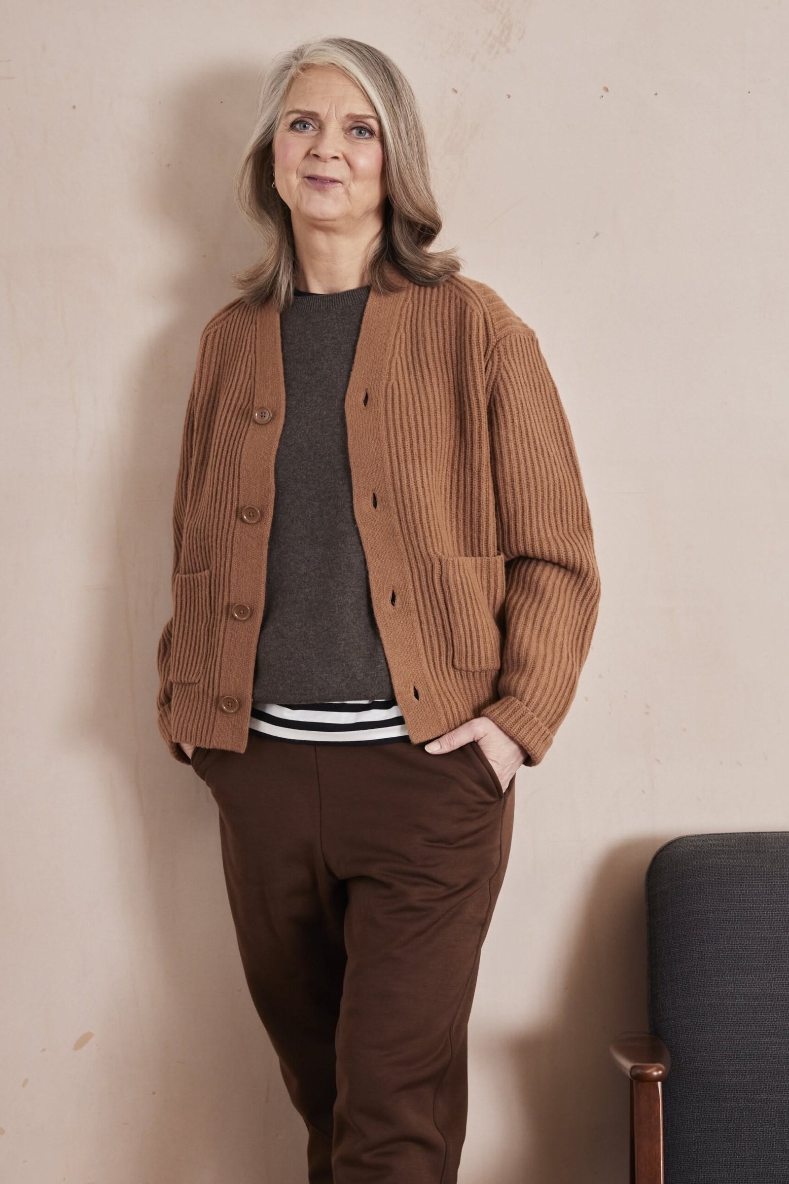 Woman leaning indoors wearing a camel cardigan with brown pants