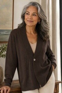 Older woman with gray-streaked hair indoors wearing a dark brown cardigan
