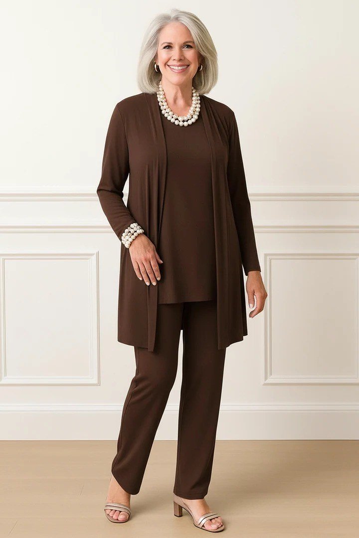 Older white-haired woman in a studio wearing a chocolate brown cardigan set with pearls