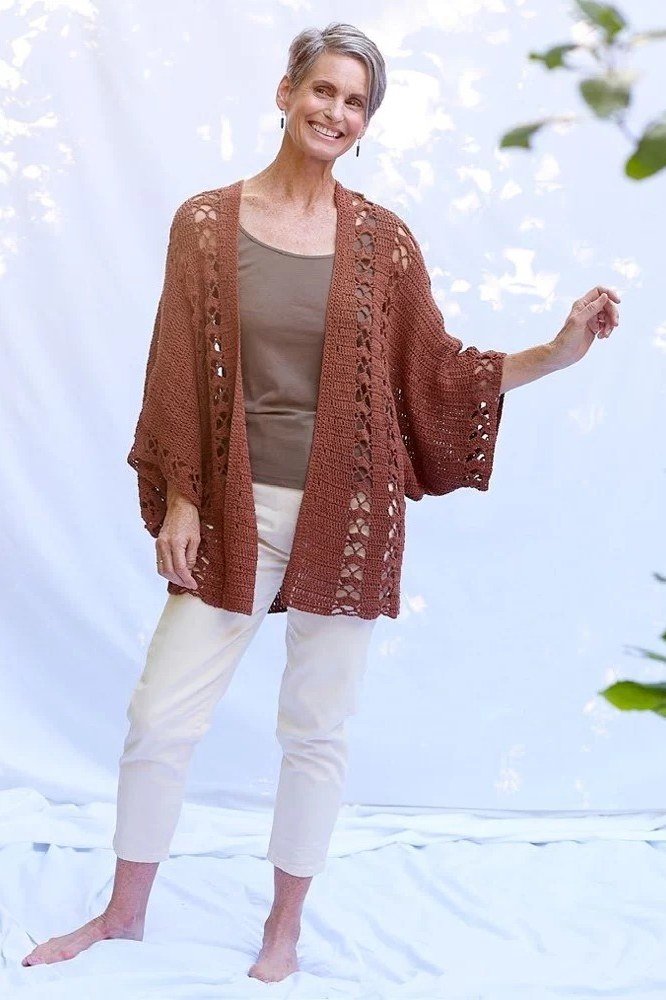 Older woman in a studio wearing a rust crochet cardigan with white capri pants