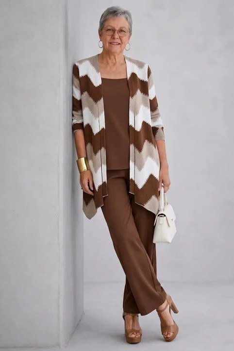 Older woman with glasses wearing a brown and white chevron cardigan with brown pants