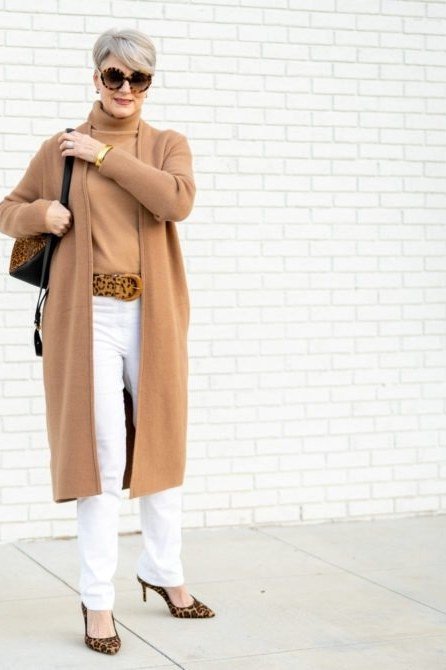 Older woman with sunglasses on a street wearing a camel long cardigan with white pants