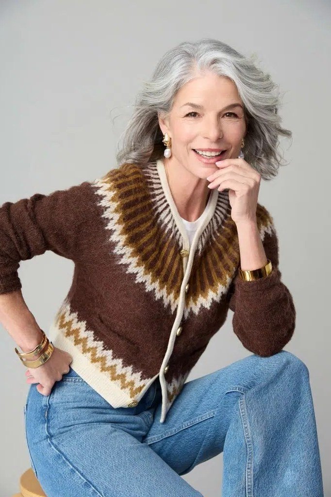 Older gray-haired woman seated, wearing a brown fair-isle yoke cardigan with jeans