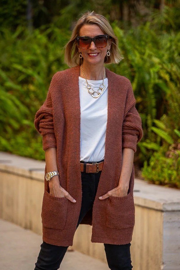 Woman with sunglasses in a garden wearing a rust cardigan over a white top