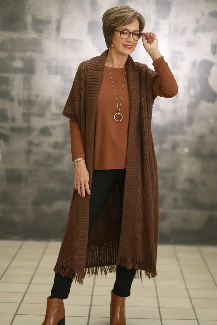 Woman in a studio wearing a rust poncho-style cardigan with black pants