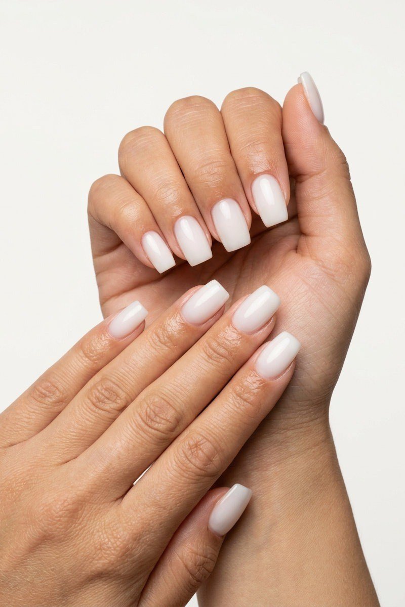 Short white builder gel nails, hands crossed, clean minimal manicure over 50