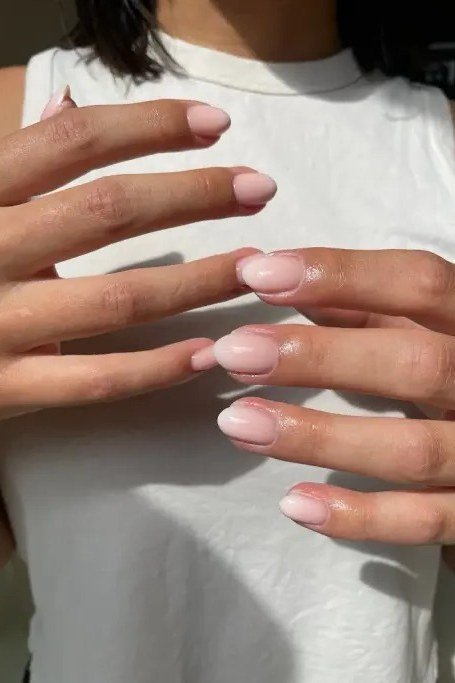 Milky French on short nails, hands on chest over white top, builder gel over 50