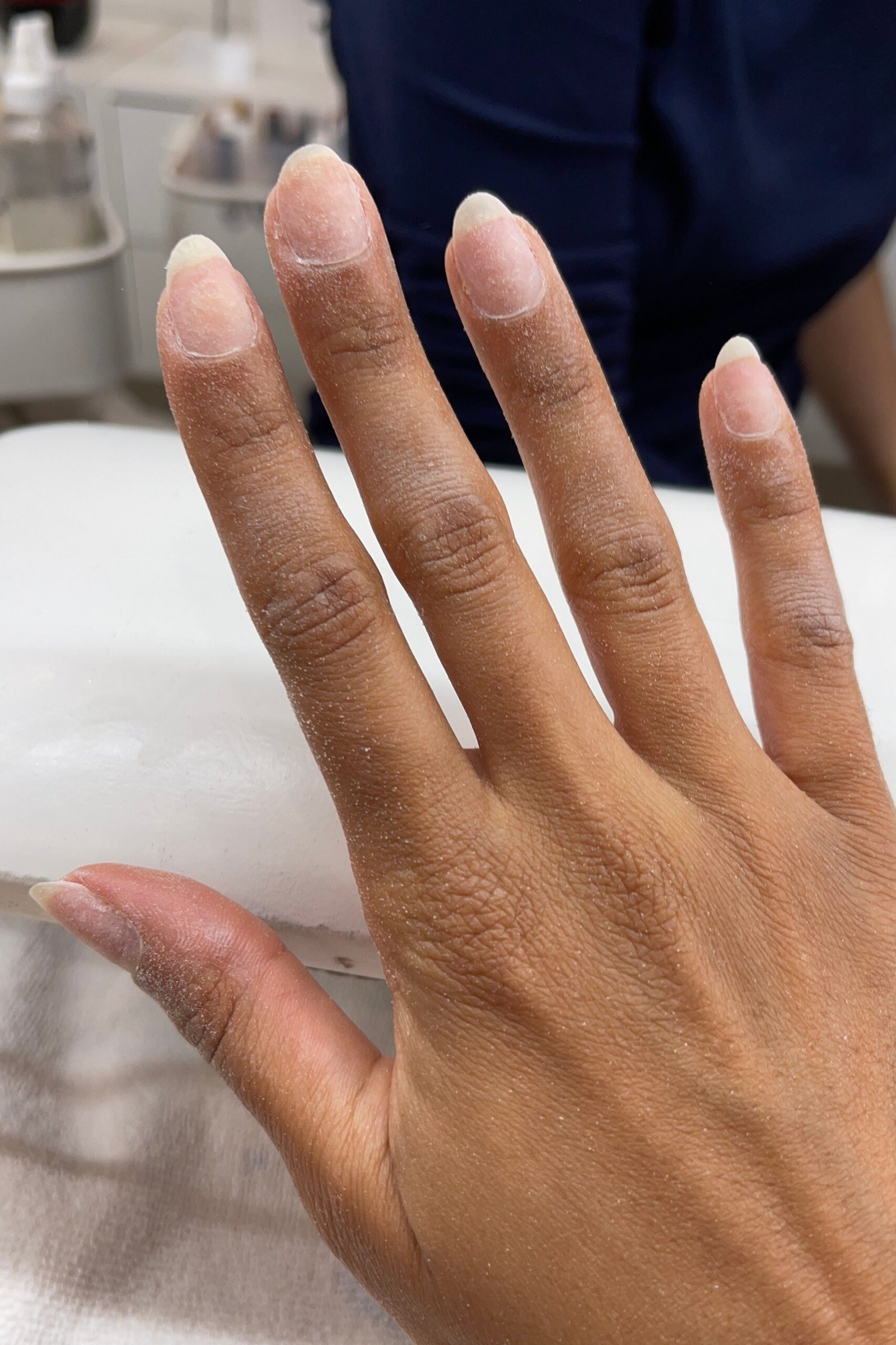 Natural nude gel overlay on dark skin hand at salon desk, builder gel over 50