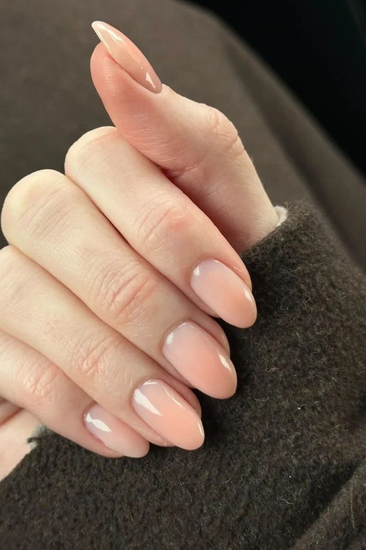 Nude almond nails on hand with brown sleeve, builder gel manicure