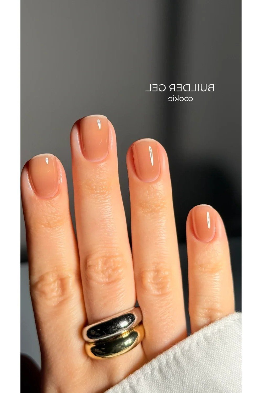 Short nude square nails with rings on dark background, builder gel over 50