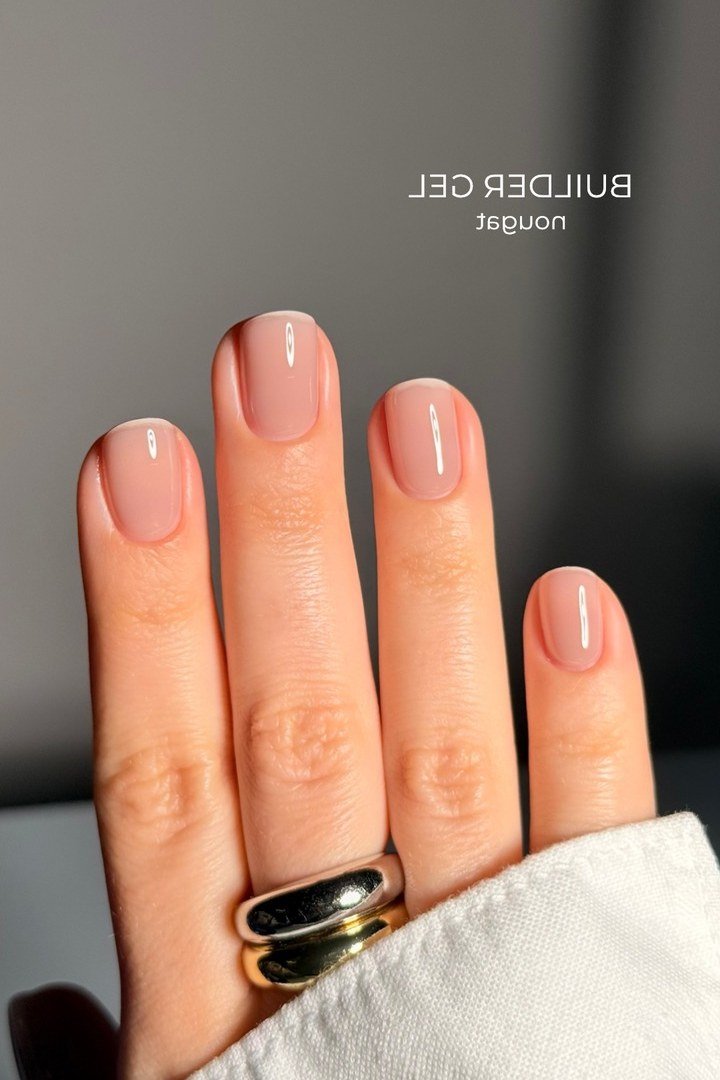Short nude nails with rings on dark background, builder gel manicure