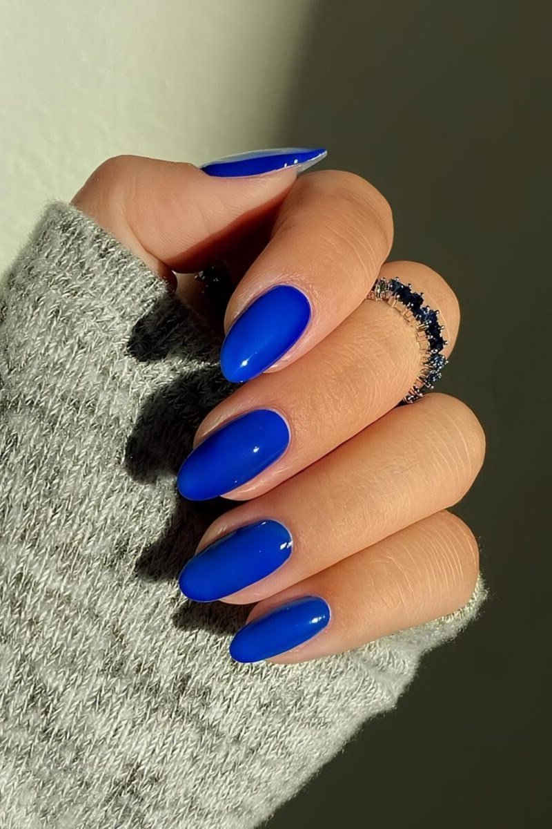 Cobalt blue almond nails on a woman over 50 wearing a gray sweater