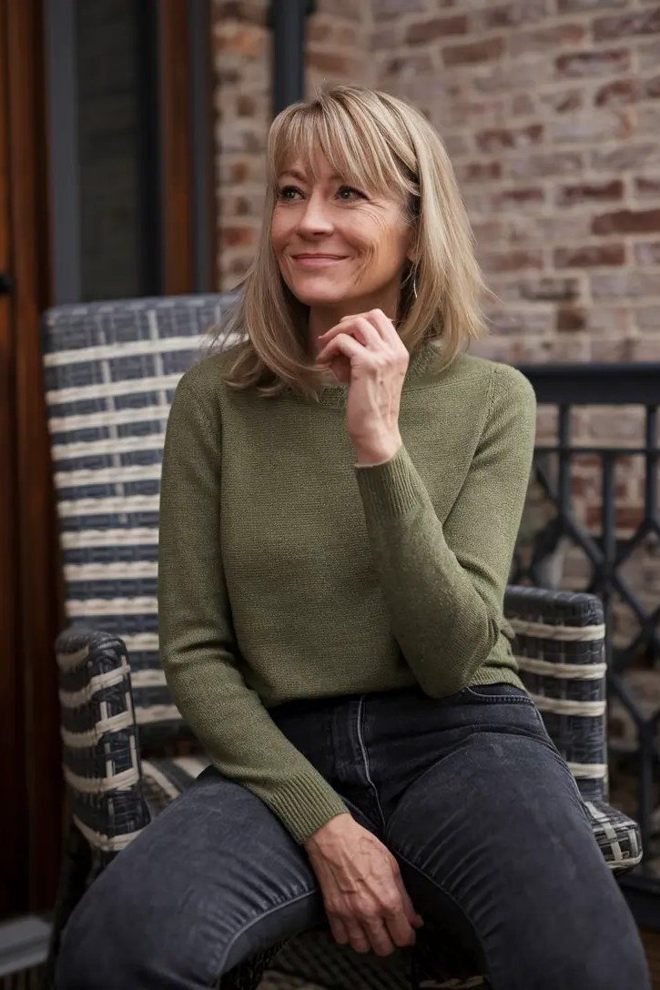 Olive sweater with dark jeans casual seated outfit for women over 40