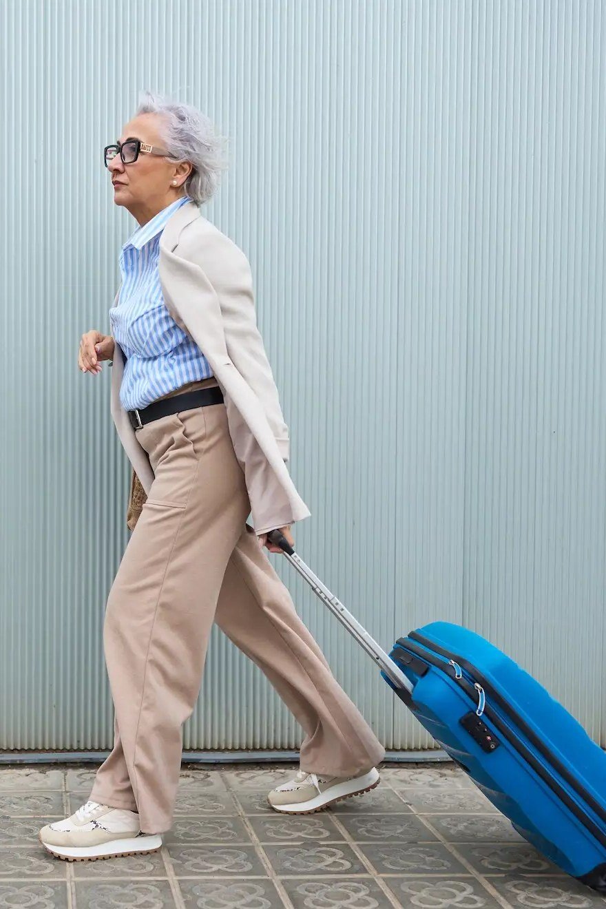 Beige top, tan wide-leg pants, blue suitcase, airport, casual outfit for women over 50
