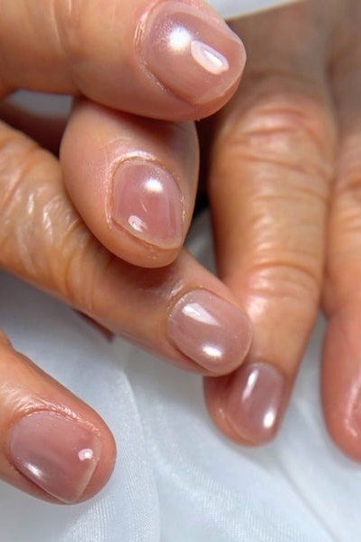 Mauve shimmer polish on short nails in a closeup of mature hands. The finish has a soft metallic glow for women over 60