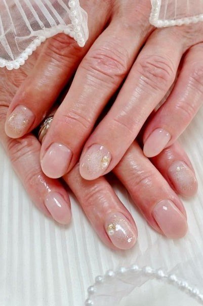 Sheer champagne-nude polish with subtle shimmer accent nails. Aged hands rest near a white lace veil for women over 60
