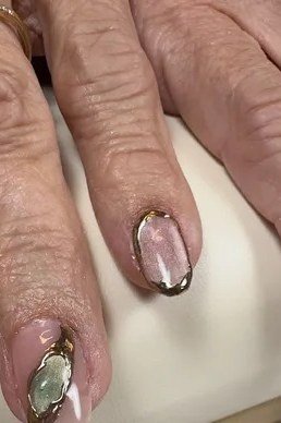 Sheer shimmer nude with delicate gold and pale green nail art motifs. Closeup of aged hands for women over 60