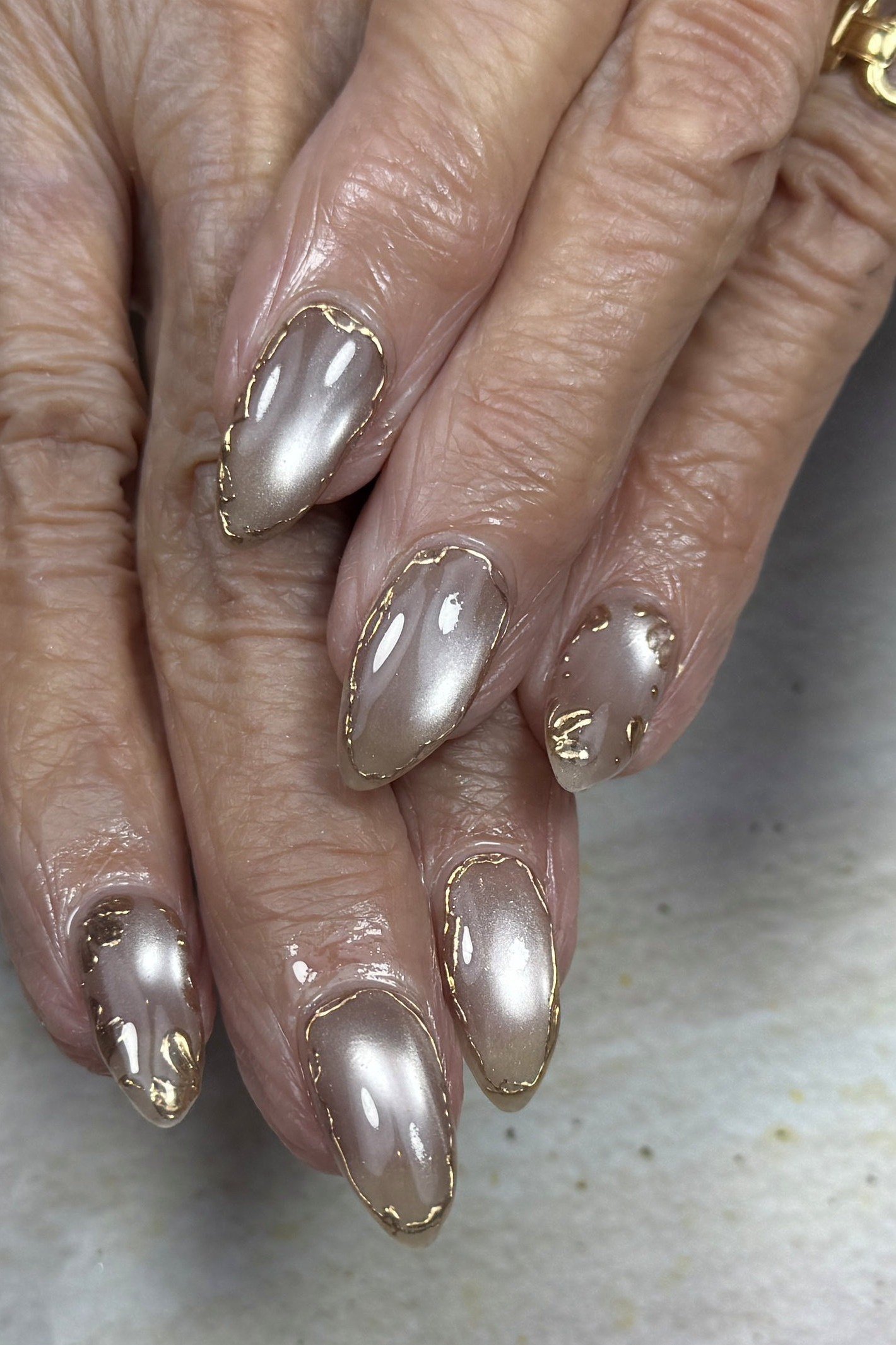 Pearl silver chrome polish on short nails of aged hands. Cool metallic finish for women over 60