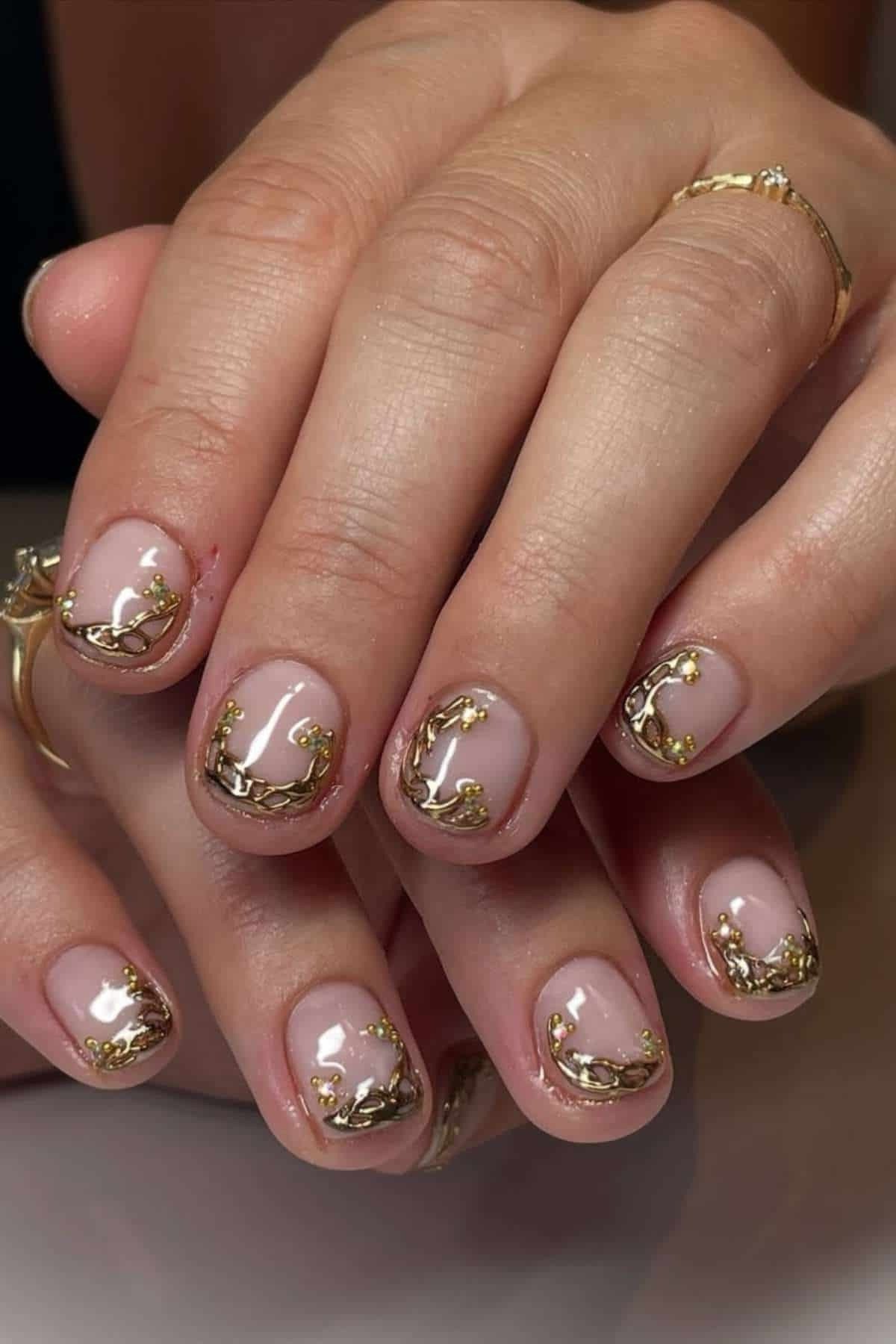 Nude polish with gold foil flake accents on short nails. Aged hands wearing gold rings for women over 60