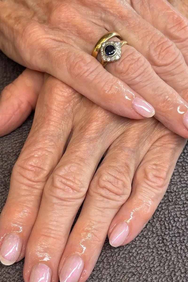 Sheer nude natural polish on aged hands, one wearing a ring. Dark background for women over 60
