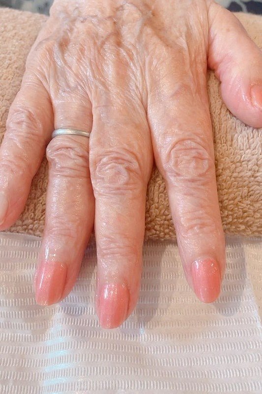 Sheer pink polish on short nails of an aged hand resting on a white towel for women over 60