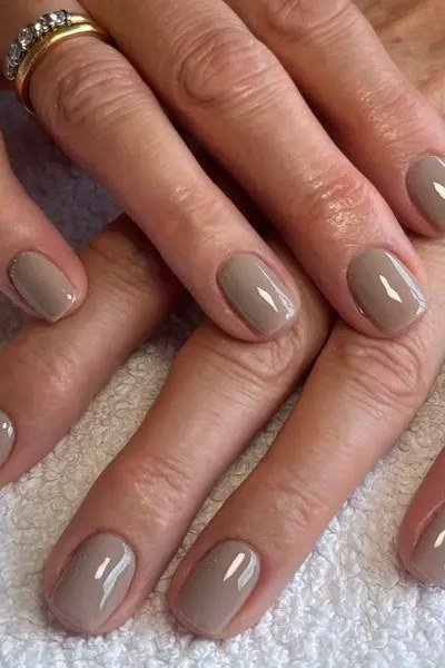 Taupe grey polish on short nails of mature hands, one wearing a ring for women over 60
