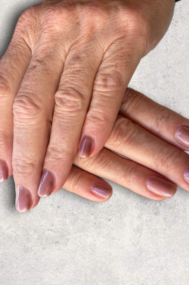 Mauve shimmer polish on short nails of aged hands. Soft satin glow for women over 60