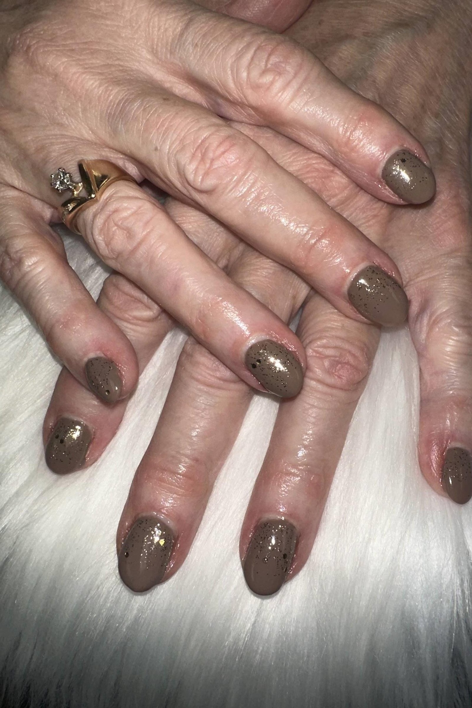 Taupe shimmer polish on short nails of aged hands wearing a ring, resting on white fur for women over 60