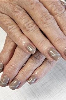 Taupe shimmer polish on short nails of aged hands. Warm metallic sheen for women over 60
