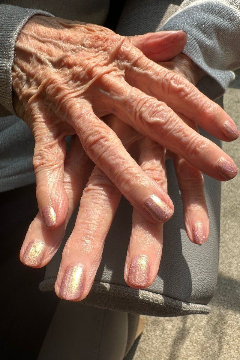 Gold shimmer polish on short nails of very aged hands. Warm antique glow for women over 60