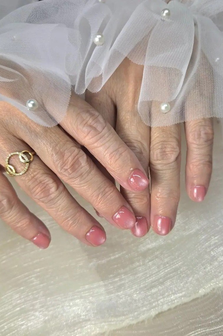 Soft pink bridal-style polish on mature hands styled with a white veil prop for women over 60