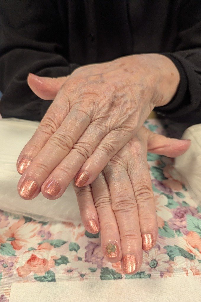 Copper shimmer polish on short nails of aged hands resting on a floral fabric for women over 60