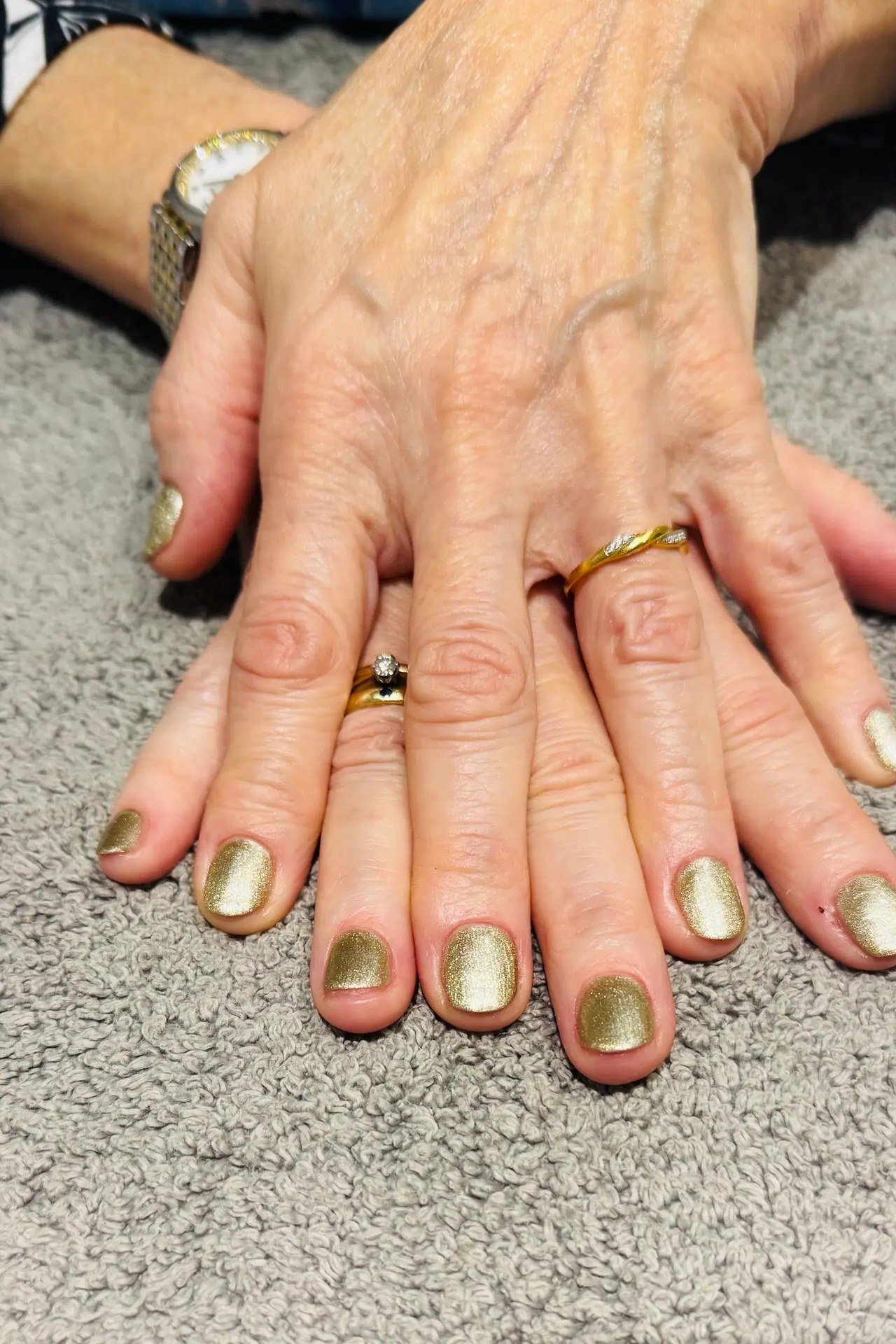 Metallic gold polish on short nails of aged hands wearing gold rings for women over 60