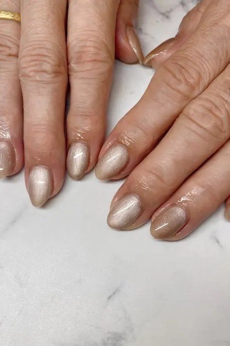Gold champagne shimmer polish on short nails of mature hands on a marble surface for women over 60
