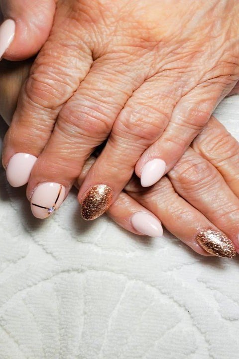 Cream polish with gold foil art accents on short nails of aged hands for women over 60