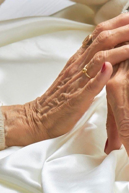 Classic red polish on short nails of aged hands resting on white satin for women over 60
