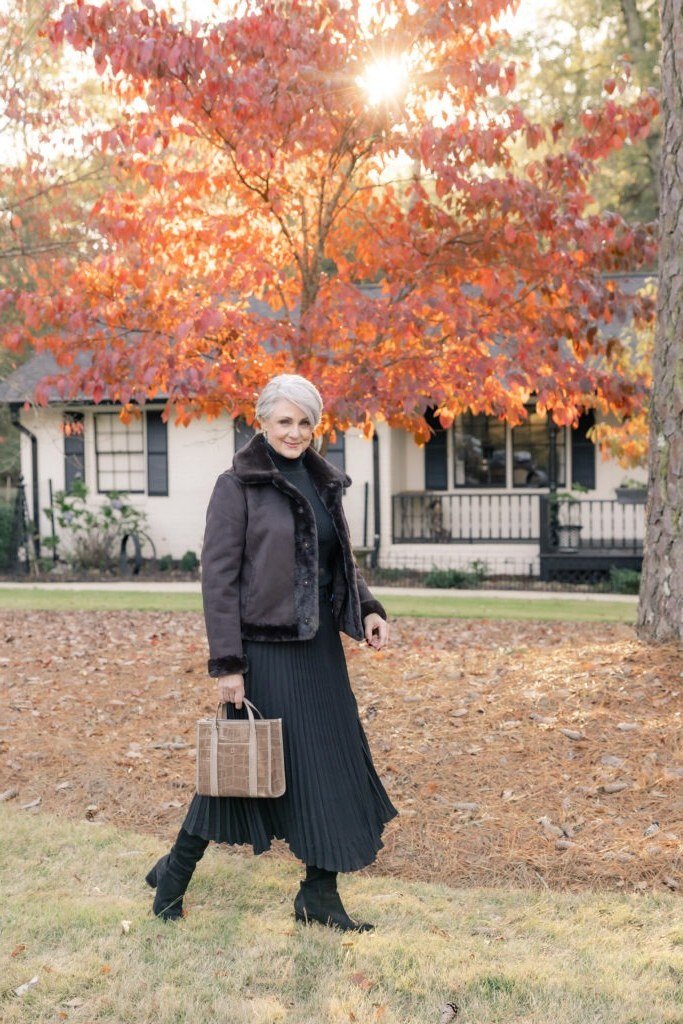 Gray-haired woman in long black coat-dress, autumn trees - classy outfit for women over 40