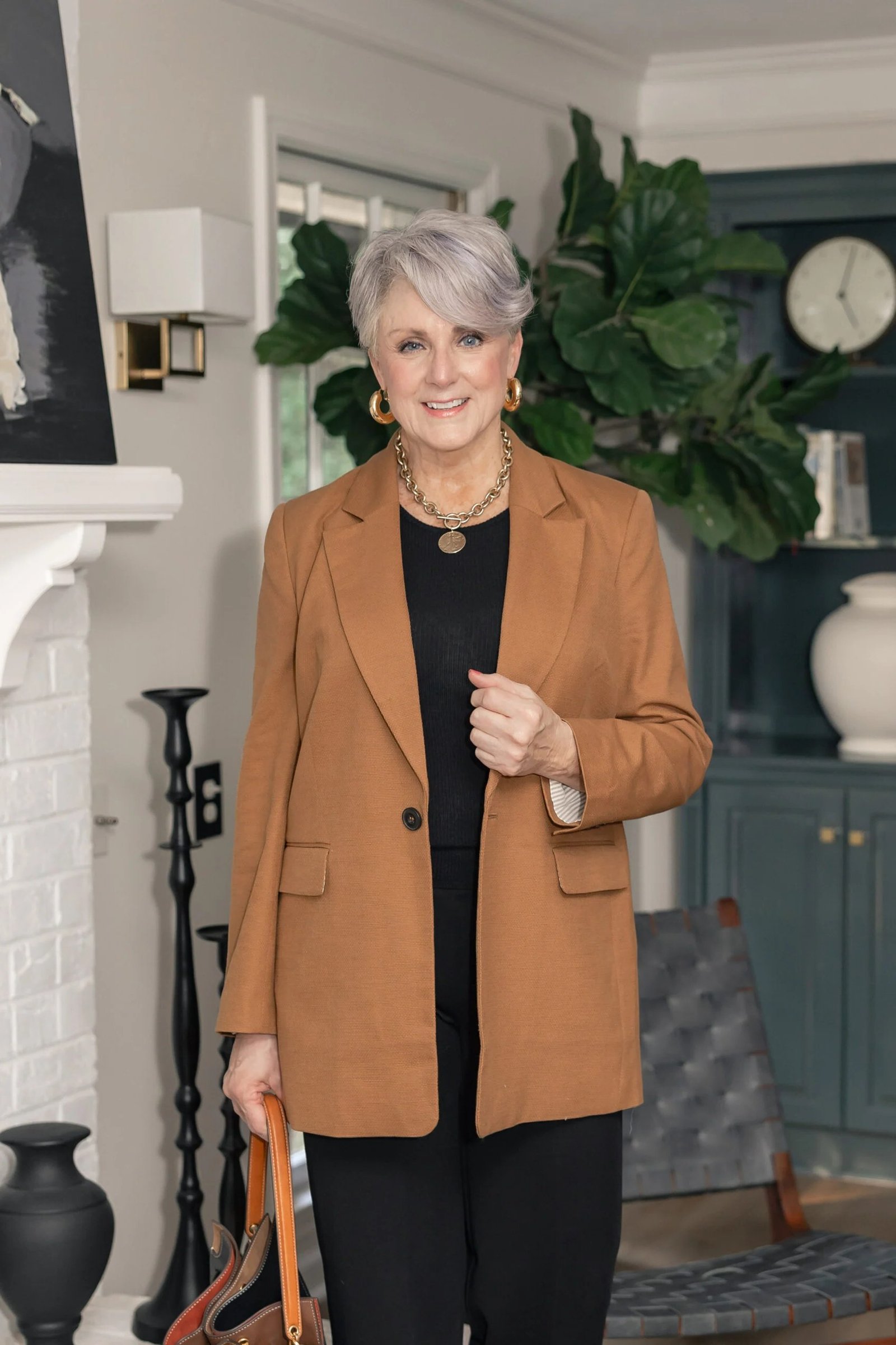 Woman over 60 wearing camel blazer, black top, dark trousers, tan bag, classy fall outfit idea