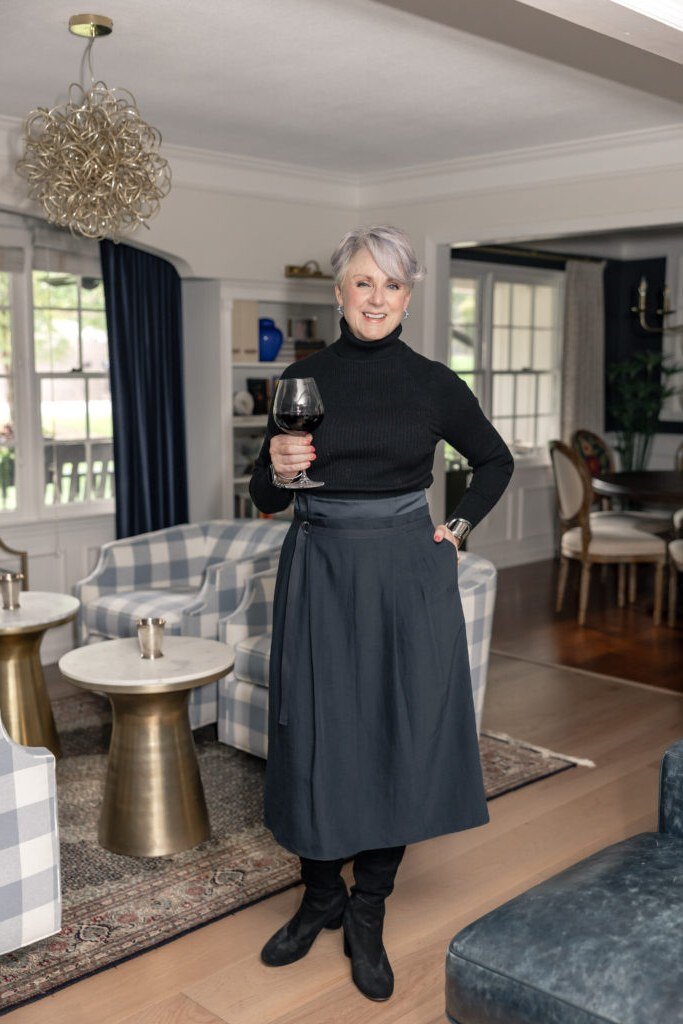 Woman over 60 wearing black turtleneck, dark midi skirt, black boots, wine glass, indoor, classy fall outfit idea