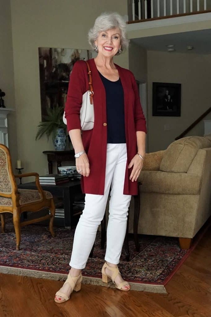 Woman over 60 wearing burgundy cardigan, navy top, white trousers, classy fall outfit idea