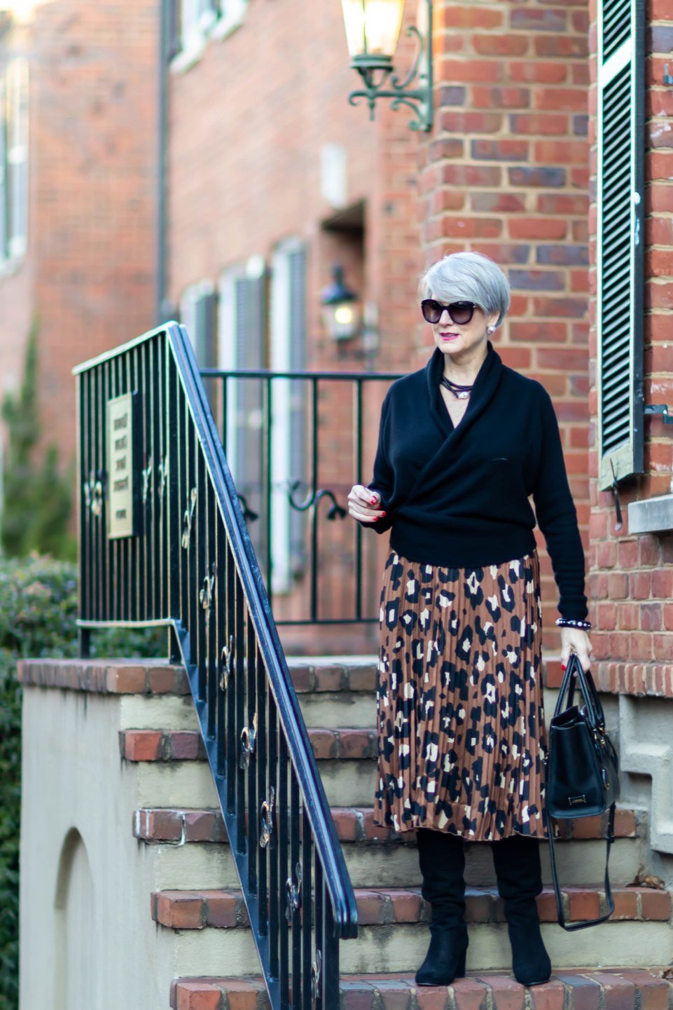 Woman over 60 wearing black top, floral midi skirt, black boots, classy fall outfit idea