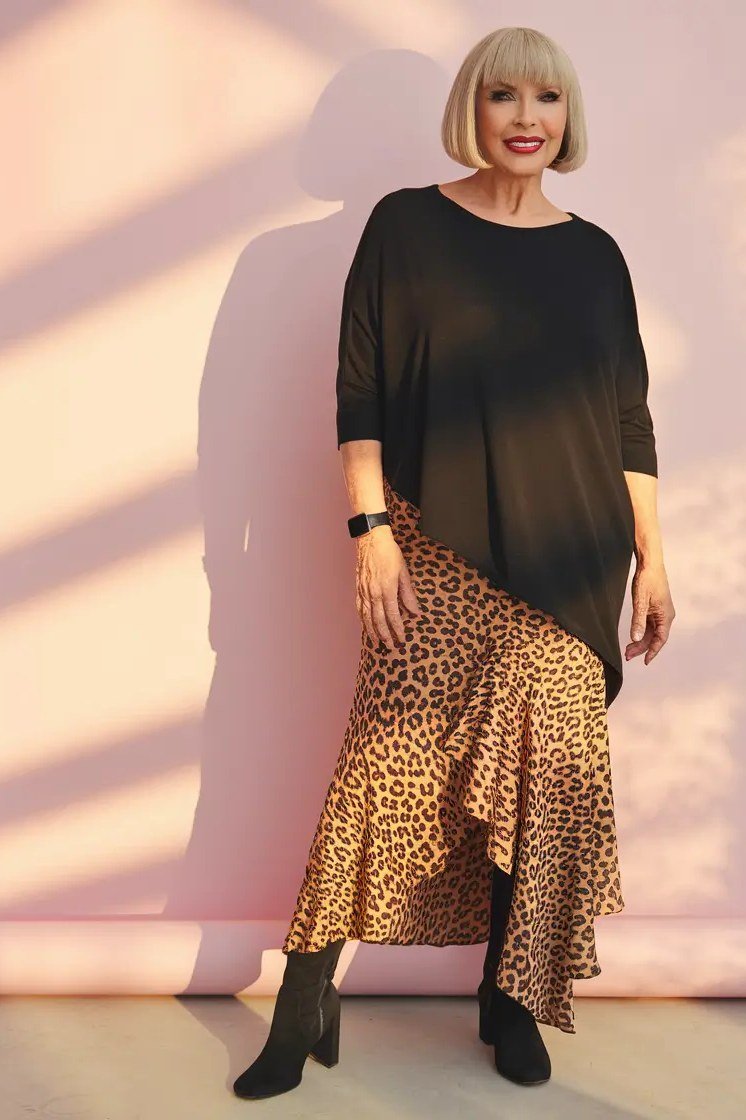 Woman over 60 wearing black top, leopard midi skirt, black boots, classy fall outfit idea