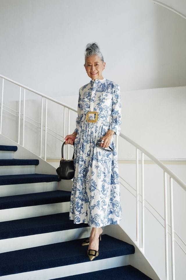 Woman over 60 wearing blue floral midi dress, black handbag, white stairs, classy fall outfit idea