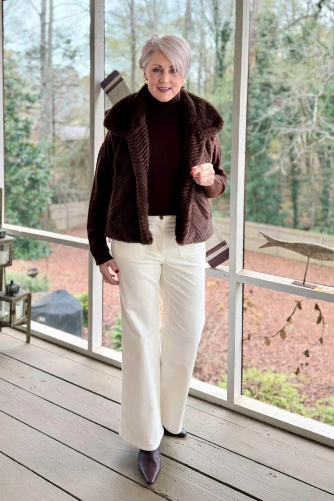 Woman over 60 wearing burgundy sweater, white wide trousers, burgundy flats, classy fall outfit idea
