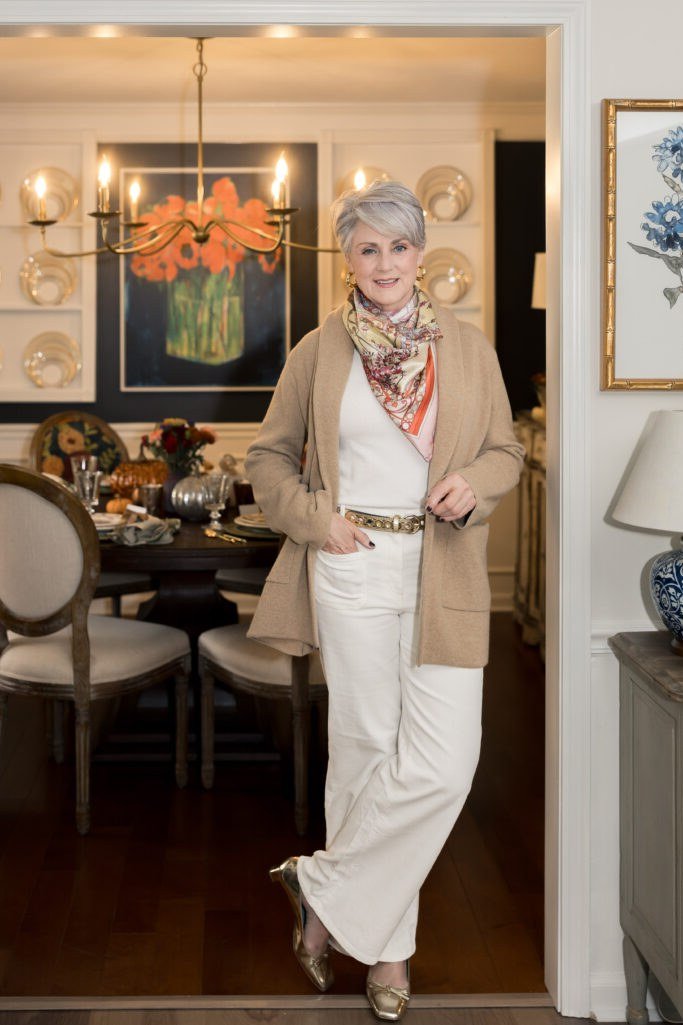 Woman over 60 wearing camel blazer, white trousers, patterned scarf, classy fall outfit idea
