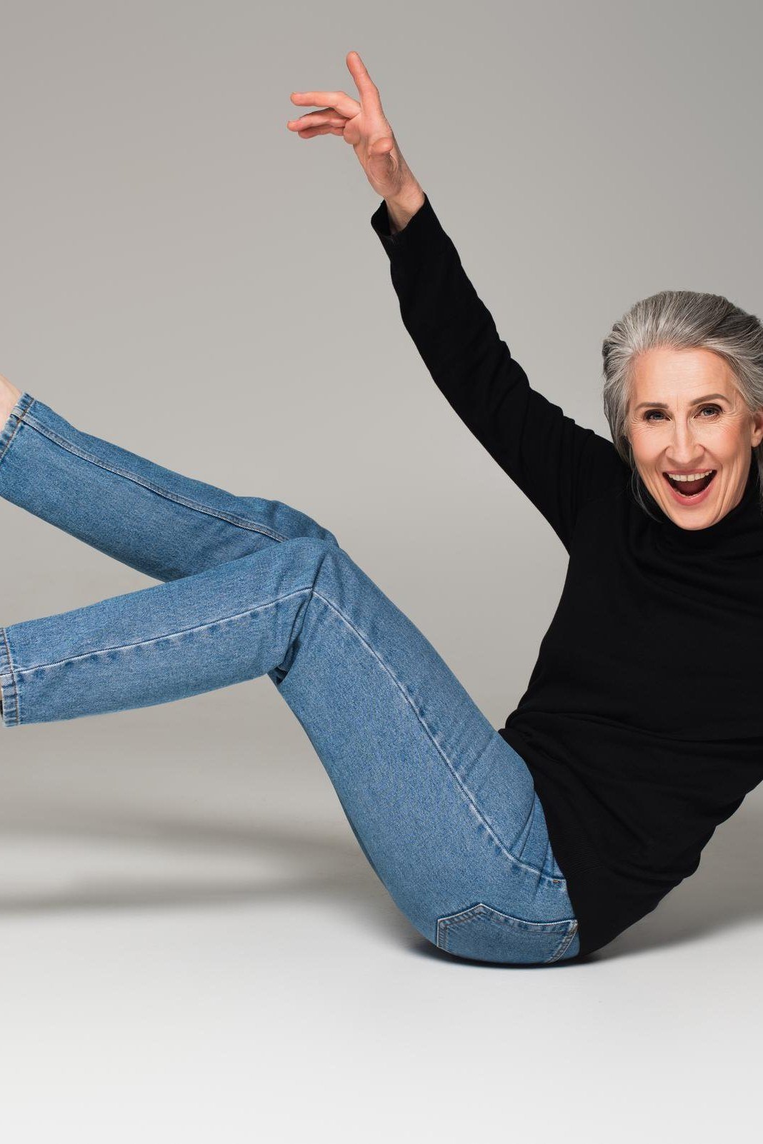 Black top with jeans in a playful jump pose, fun casual outfit for women over 50