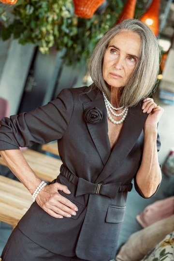 Woman over 50 in black belted blazer with layered pearls