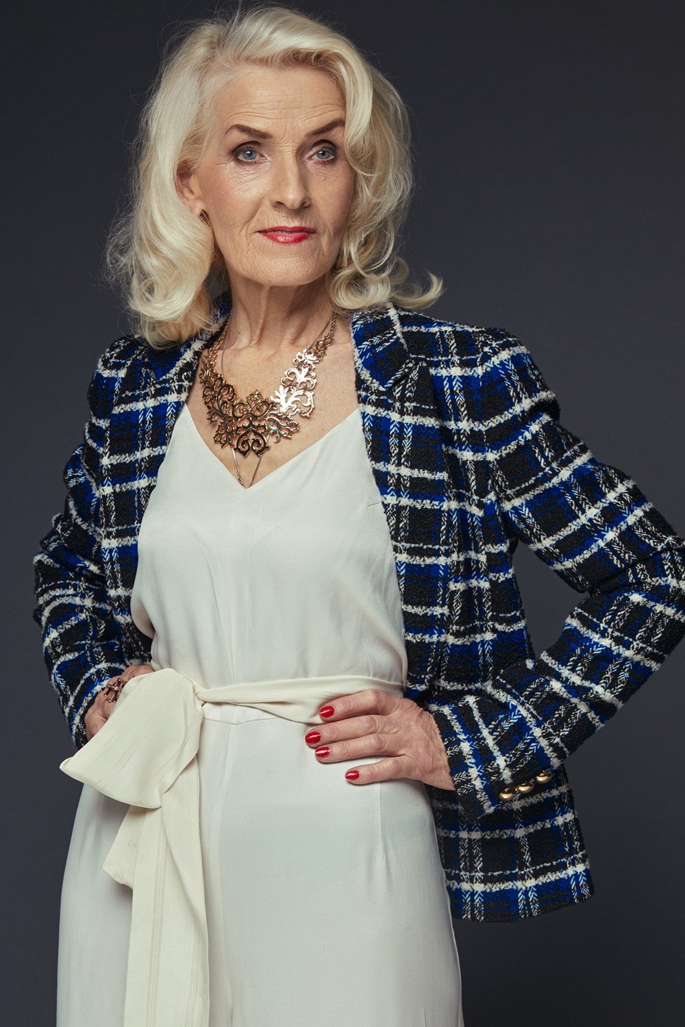 Woman over 50 in blue plaid blazer and cream tie-waist dress with statement necklace