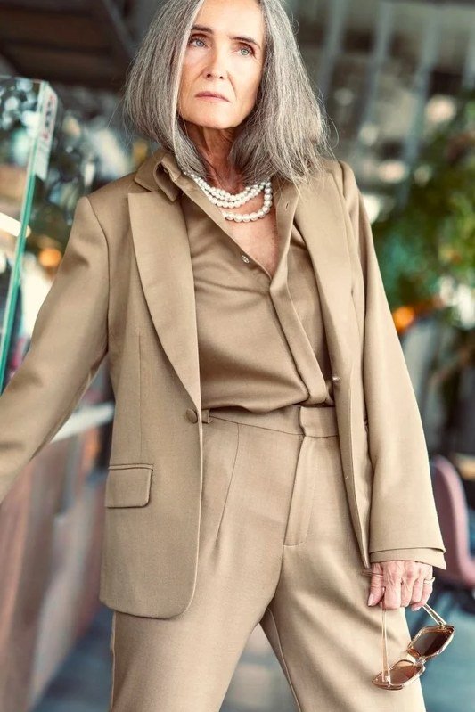Woman over 50 in tan suit with matching blouse and layered pearls