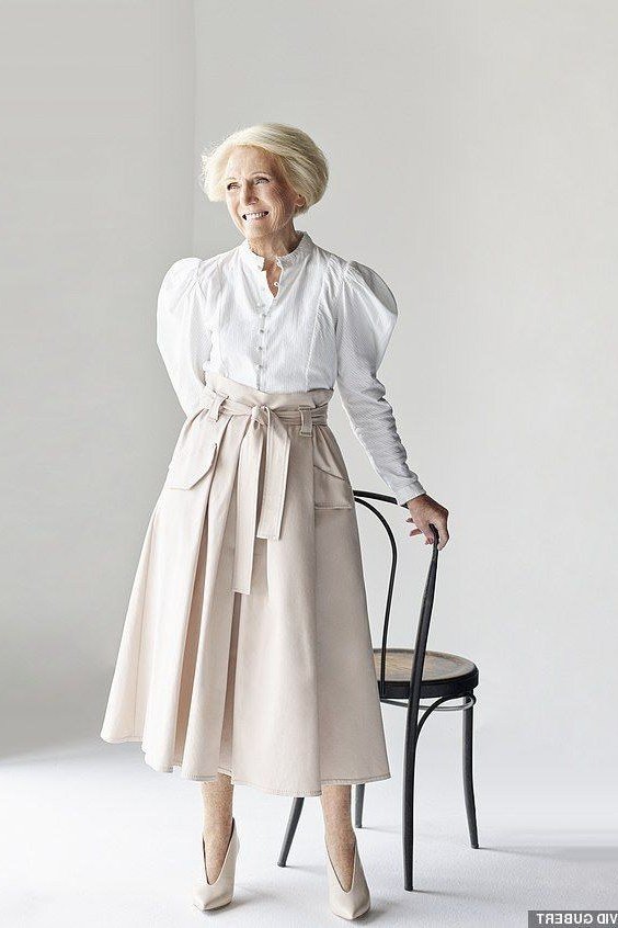 Woman over 50 in white puff-sleeve blouse and beige sash-waist midi skirt
